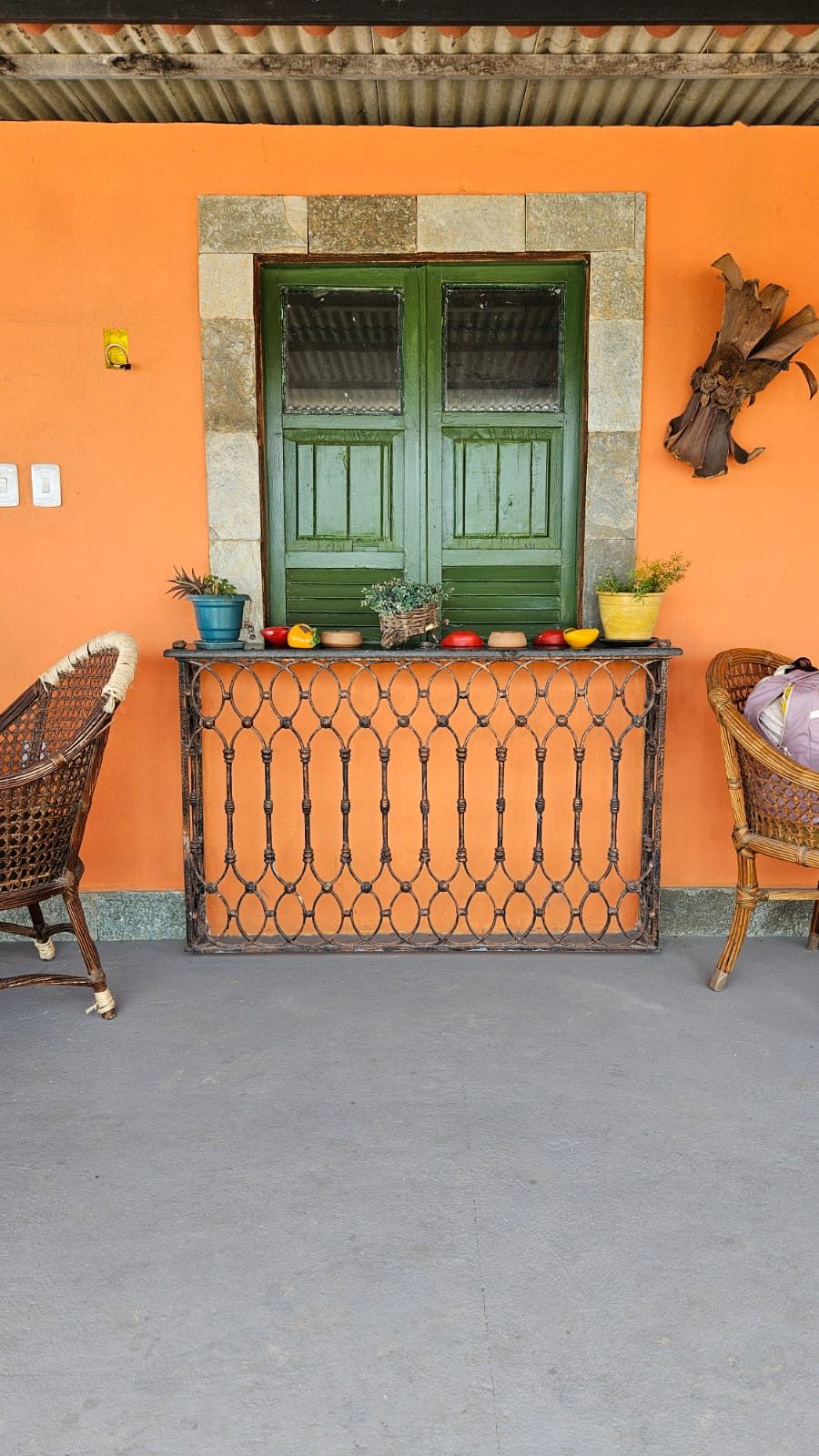 Fachada laranja do Chalés da Ribeira com janela de madeira verde, cadeiras de vime e plantas